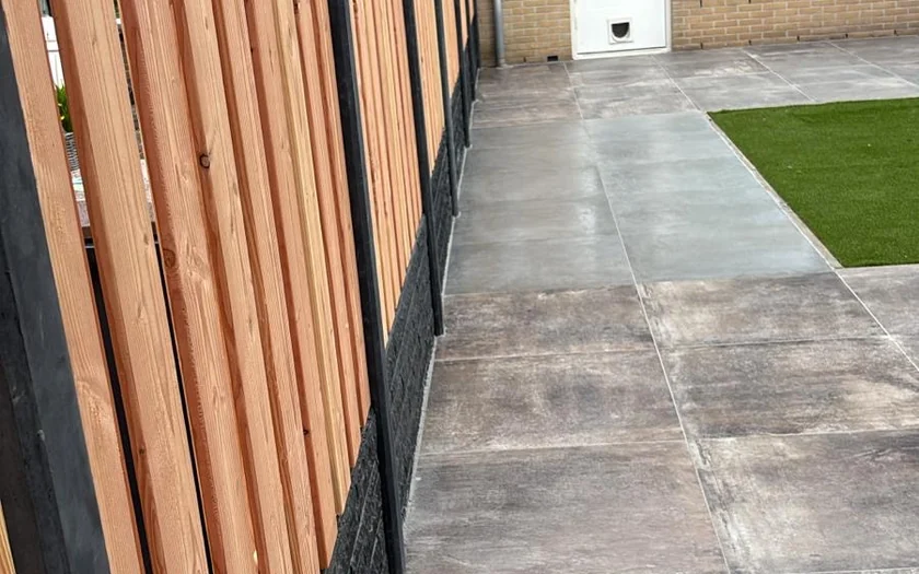 Nieuwe houten schutting op antraciet betonbanden, langs een betegeld terras
