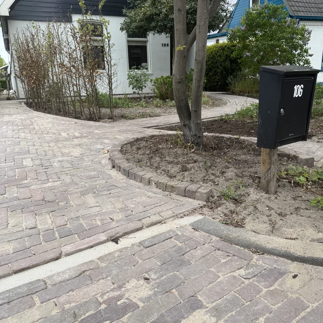 De oprit vanaf de stoep gezien, met ronde border rond de boom en brievenbus